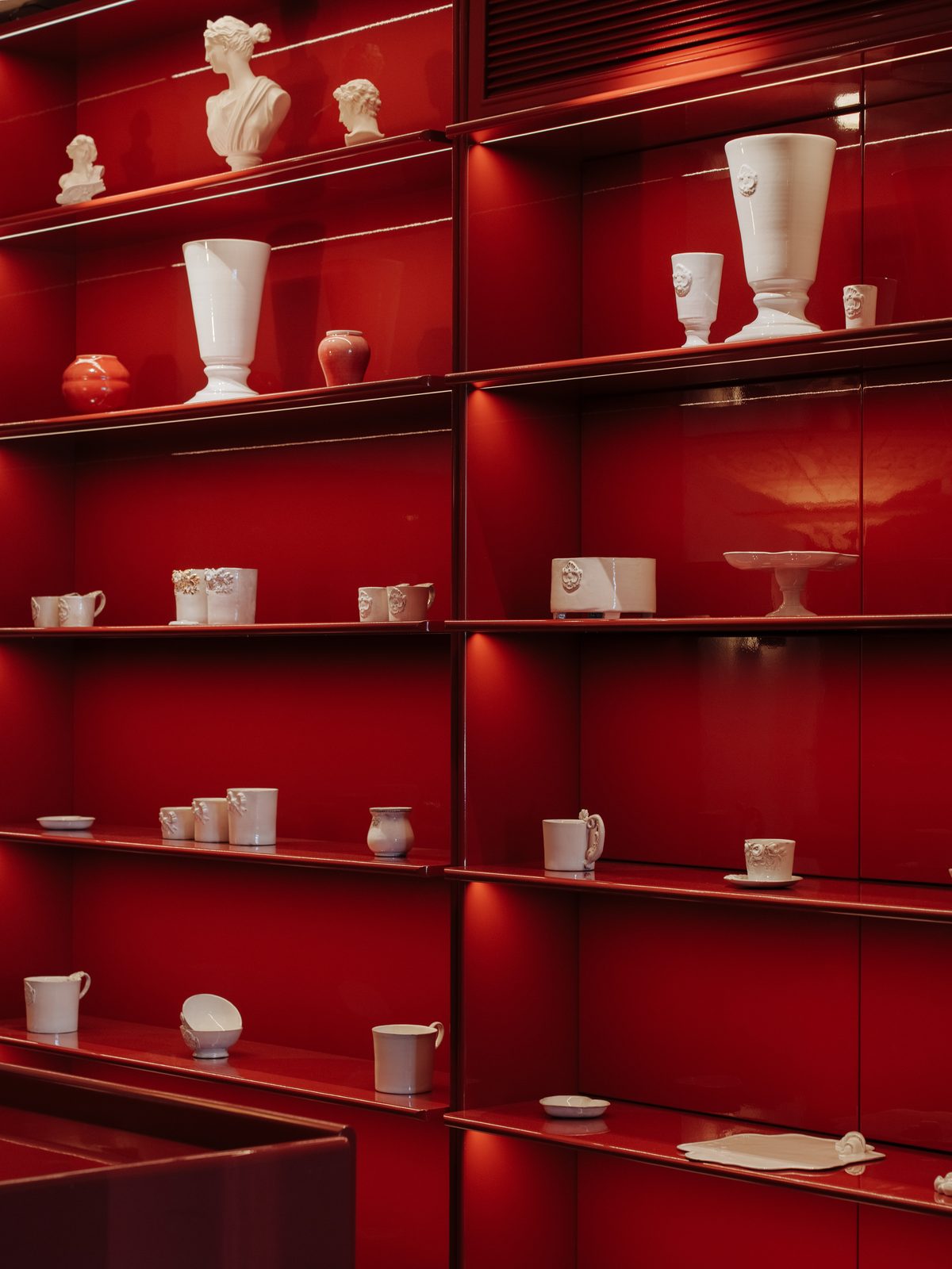 White porcelain vessels and classical busts on deep red lacquer shelves